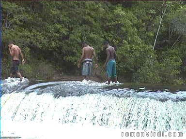 Guys wading across the waterfall