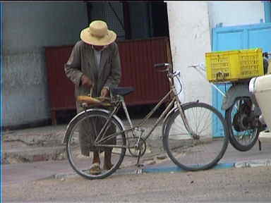 This old guy bought a bread at the bakery and he's now busy fixing it to his bike with a piece of thread