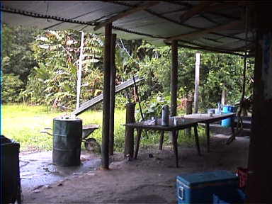 Camp is extremely rudimentary. To bathe, "use the river". You can see the contraption to collect rain water in a barrel. On the right is the 'coffee table'. There are no walls and hence no doors.